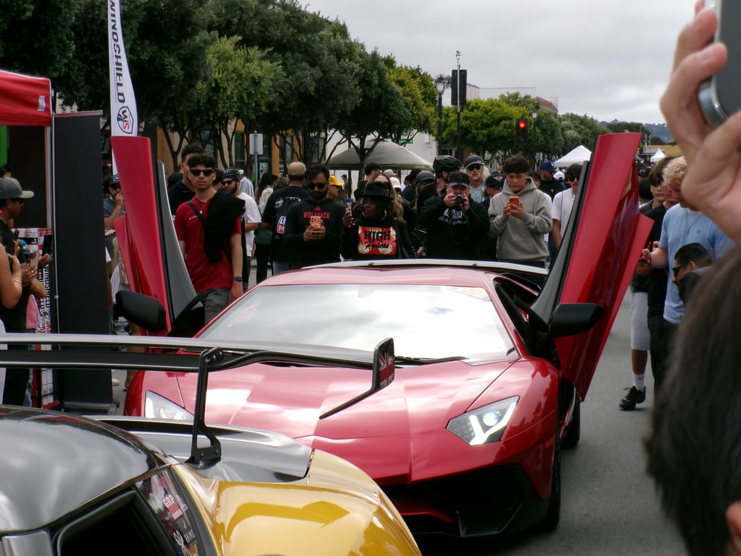 red lamborghini aventador with both doors up on a closed street, a crowd holding up phones