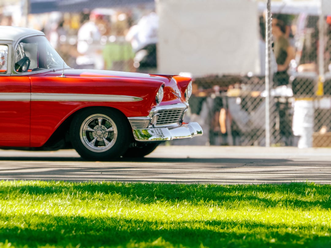 red and white chevy bel air rolling past a chain-link fence, bright green grass in front