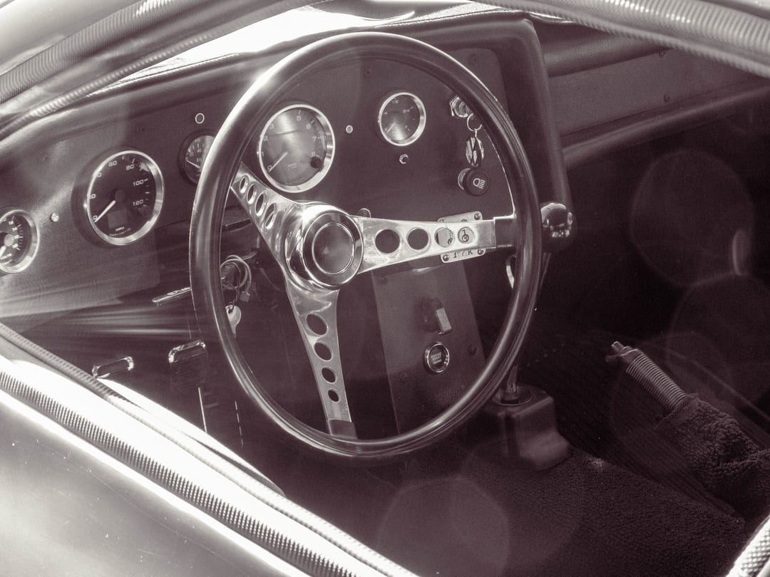 drilled three-spoke steering wheel and round gauges of a vintage race car, seen through the window in sepia