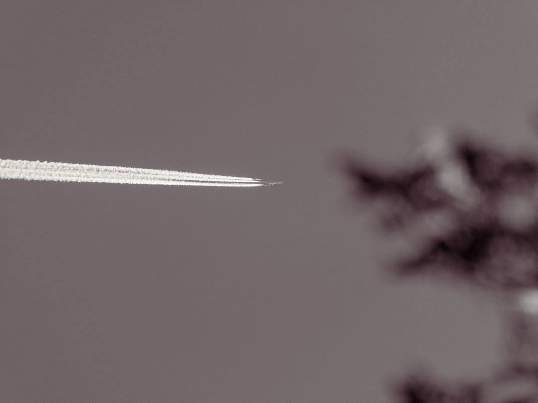 a jet drawing four white contrails across a sepia sky, blurred branches to the right