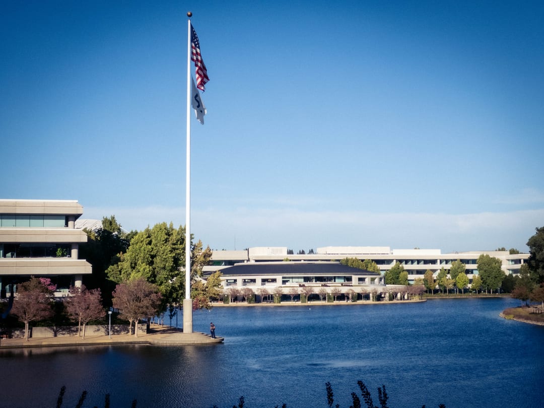 flagpole on the edge of a lake in front of low office buildings, clear blue sky