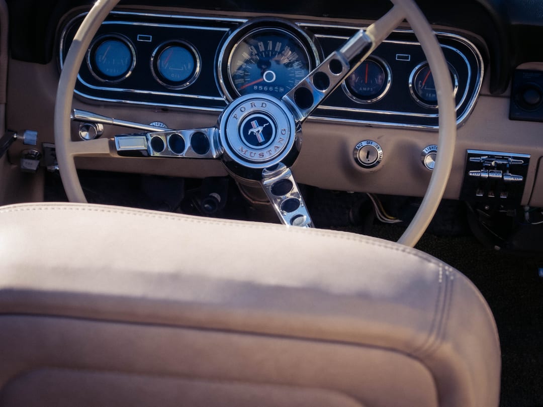 steering wheel and gauges of a classic ford mustang, cream leather seat in the foreground